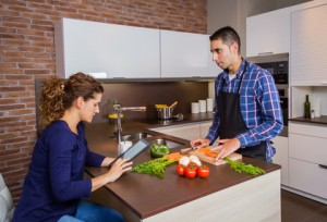 Man cooking and woman looking recipe in electronic tablet